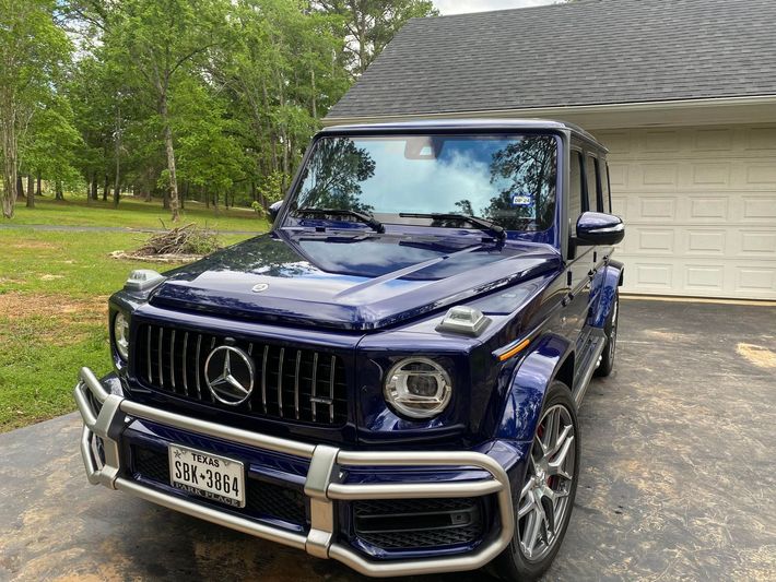 A blue mercedes benz g63 is parked in front of a garage.