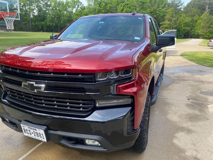 A red truck is parked in a driveway next to a basketball hoop.