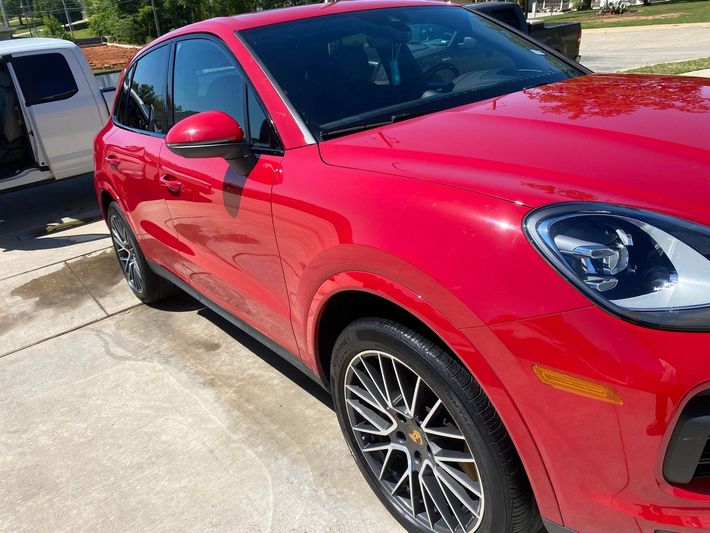 A red porsche cayenne is parked in a driveway next to a white van.