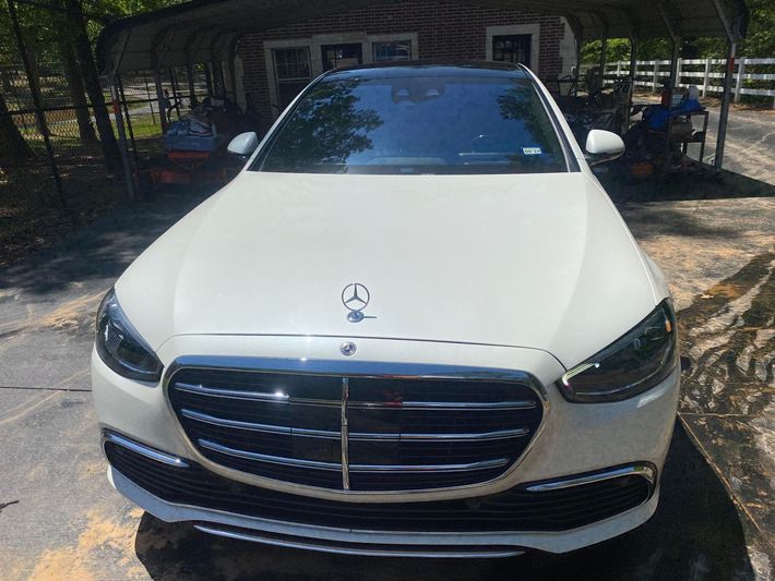 A white mercedes benz is parked in front of a carport.