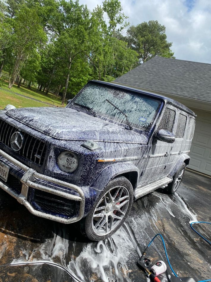 A blue jeep is covered in foam in a driveway in front of a house.