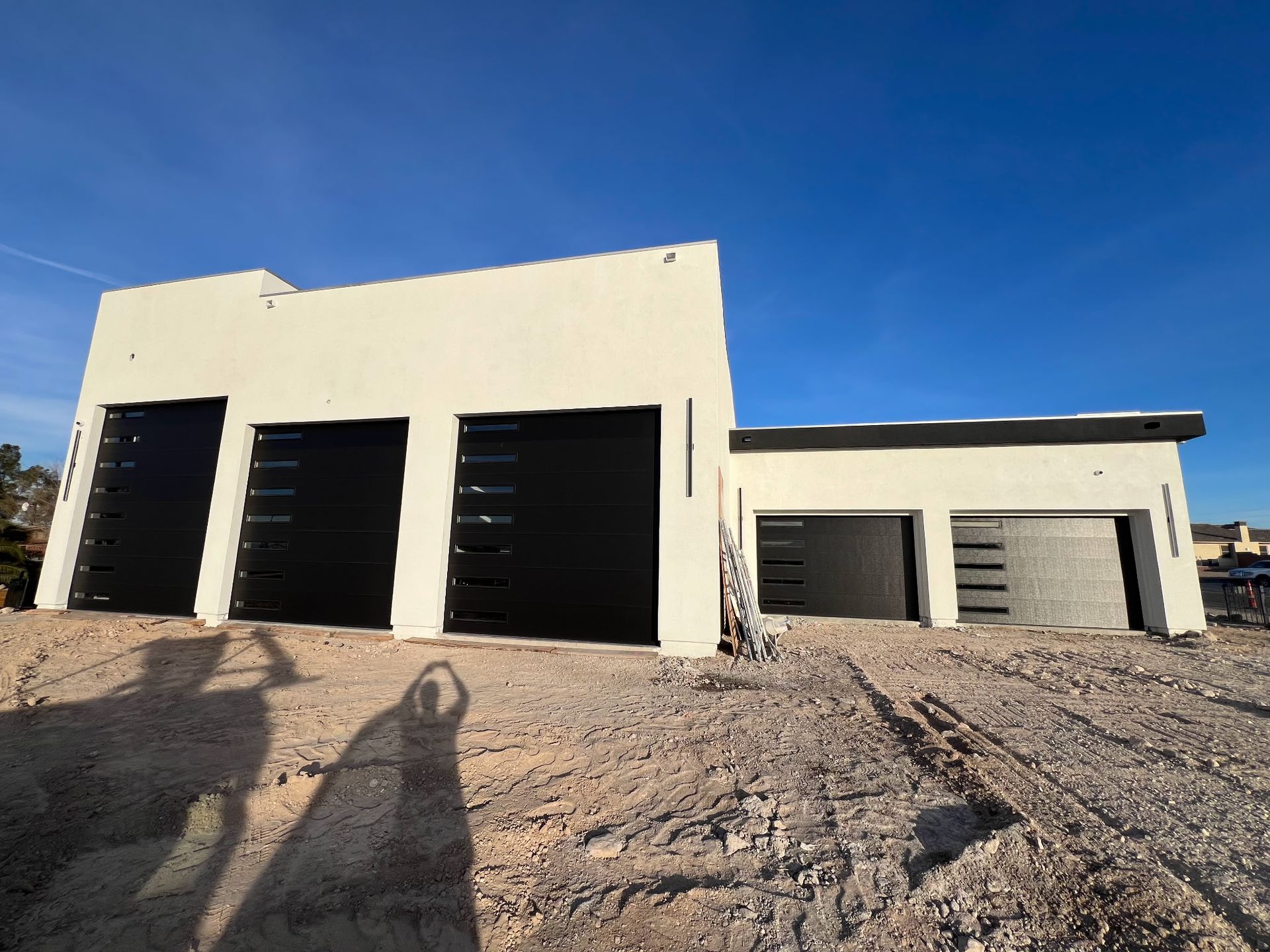 A white house with black garage doors is being built in the desert