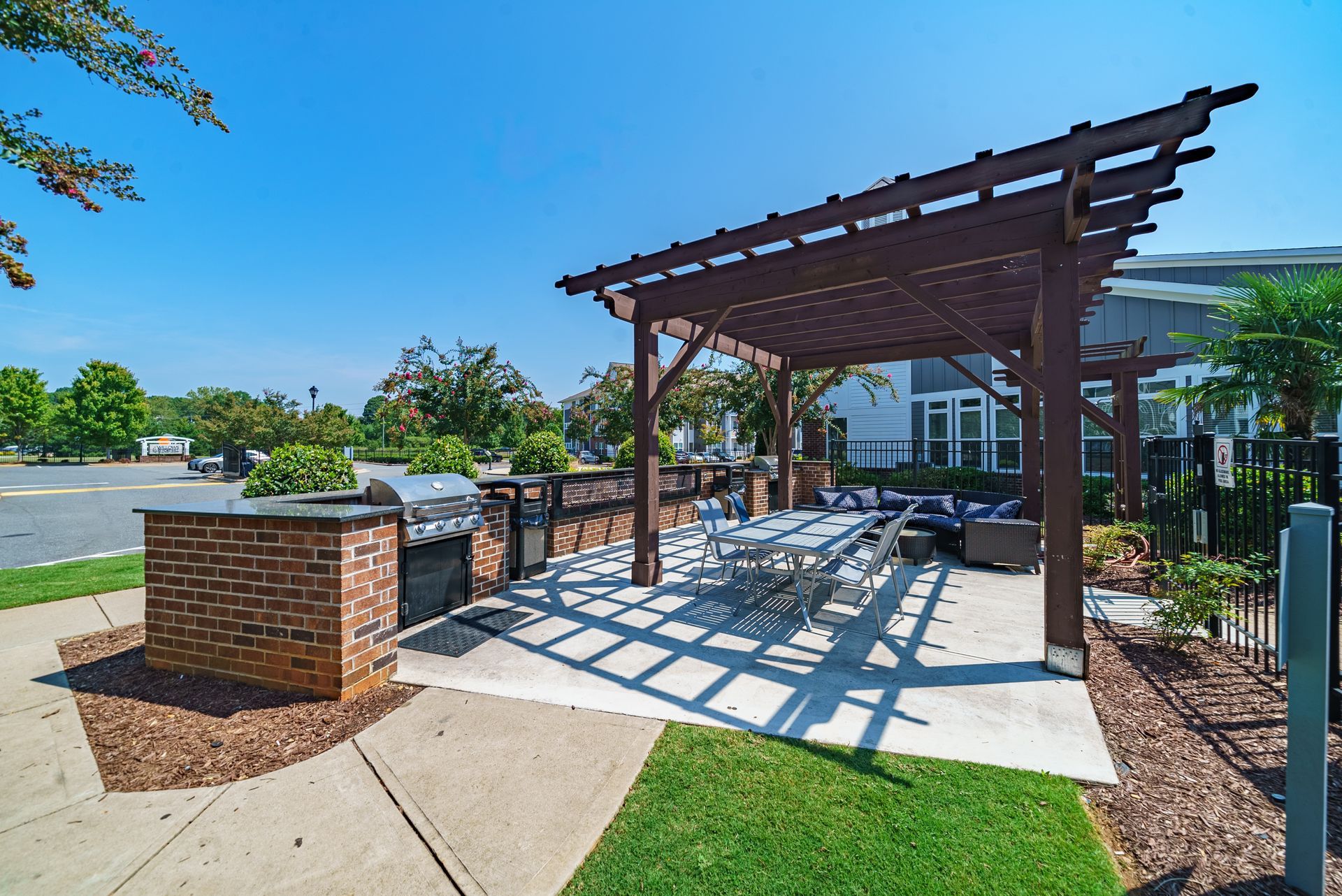 Outdoor patio with grill, pergola, seating, and brick wall against a blue sky at Willows at Fort Mill, offers apartments for rent near I-77 in Fort Mill, SC.