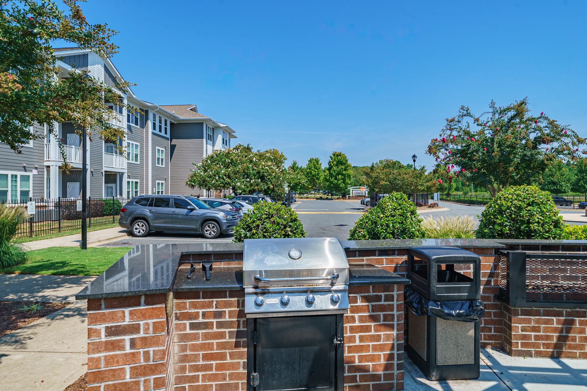 Outdoor grilling station with a stainless steel grill, trash bin, and brick counter, in front of an apartment building at Willows at Fort Mill, offers apartments for rent near Kingsley Town Center in Fort Mill, SC.