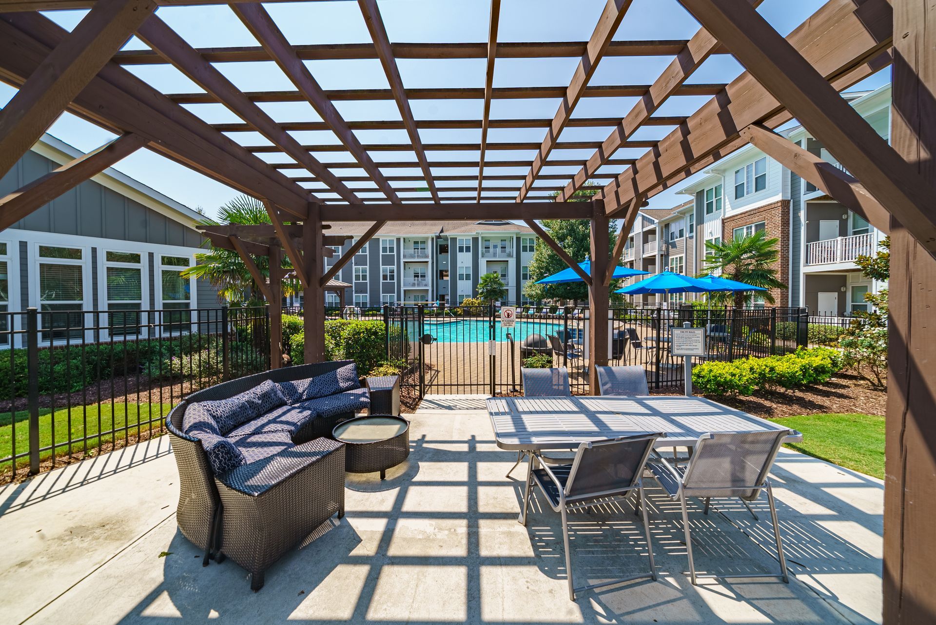 Outdoor seating area under a wooden pergola with a view of a pool and apartment buildings at Willows at Fort Mill, offers pet-friendly apartments near Downtown Fort Mill, SC.