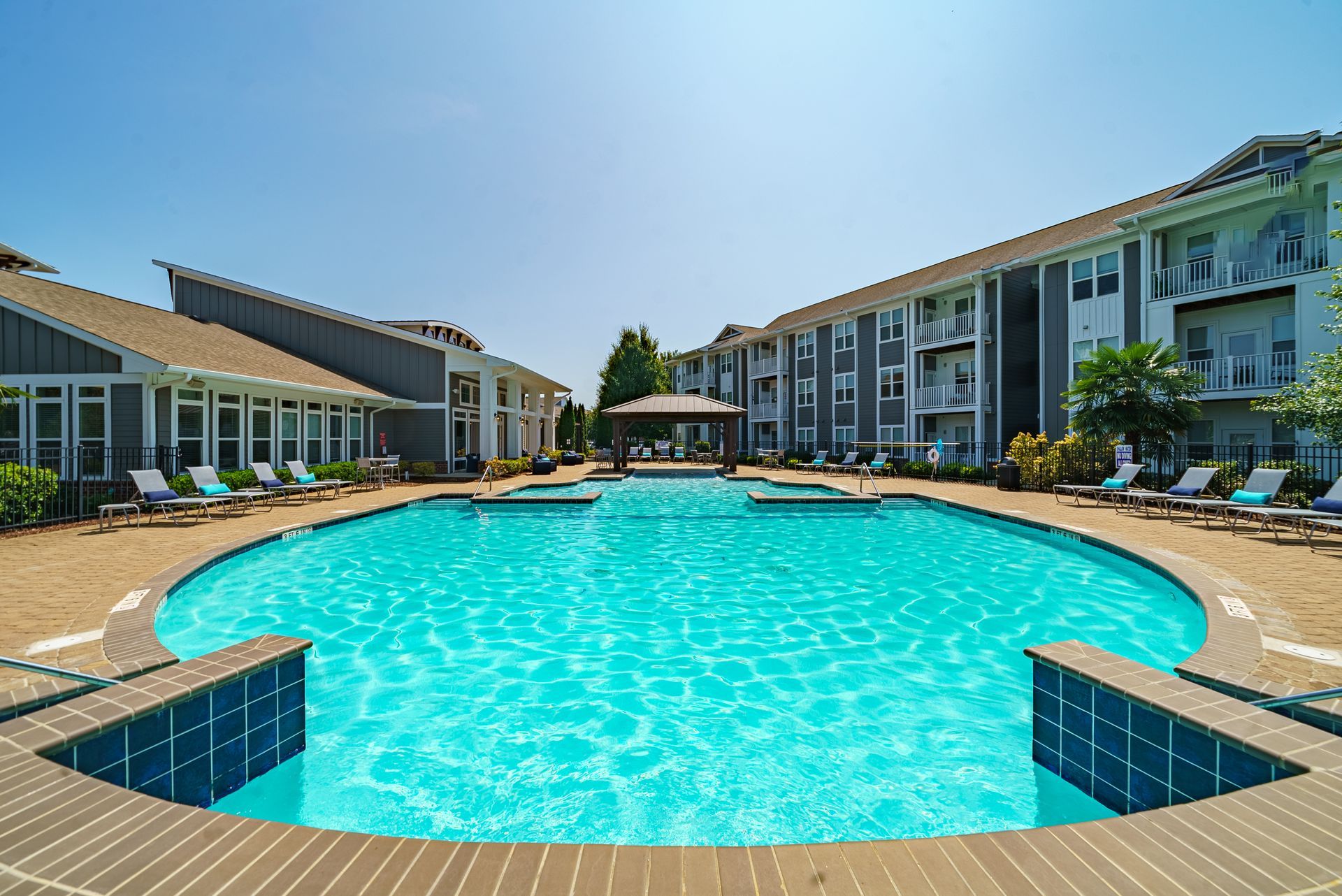 A large, turquoise pool surrounded by lounge chairs and apartment buildings on a sunny day at Willows at Fort Mill, offers 1, 2, and 3 bedroom apartments for rent in Fort Mill, SC.