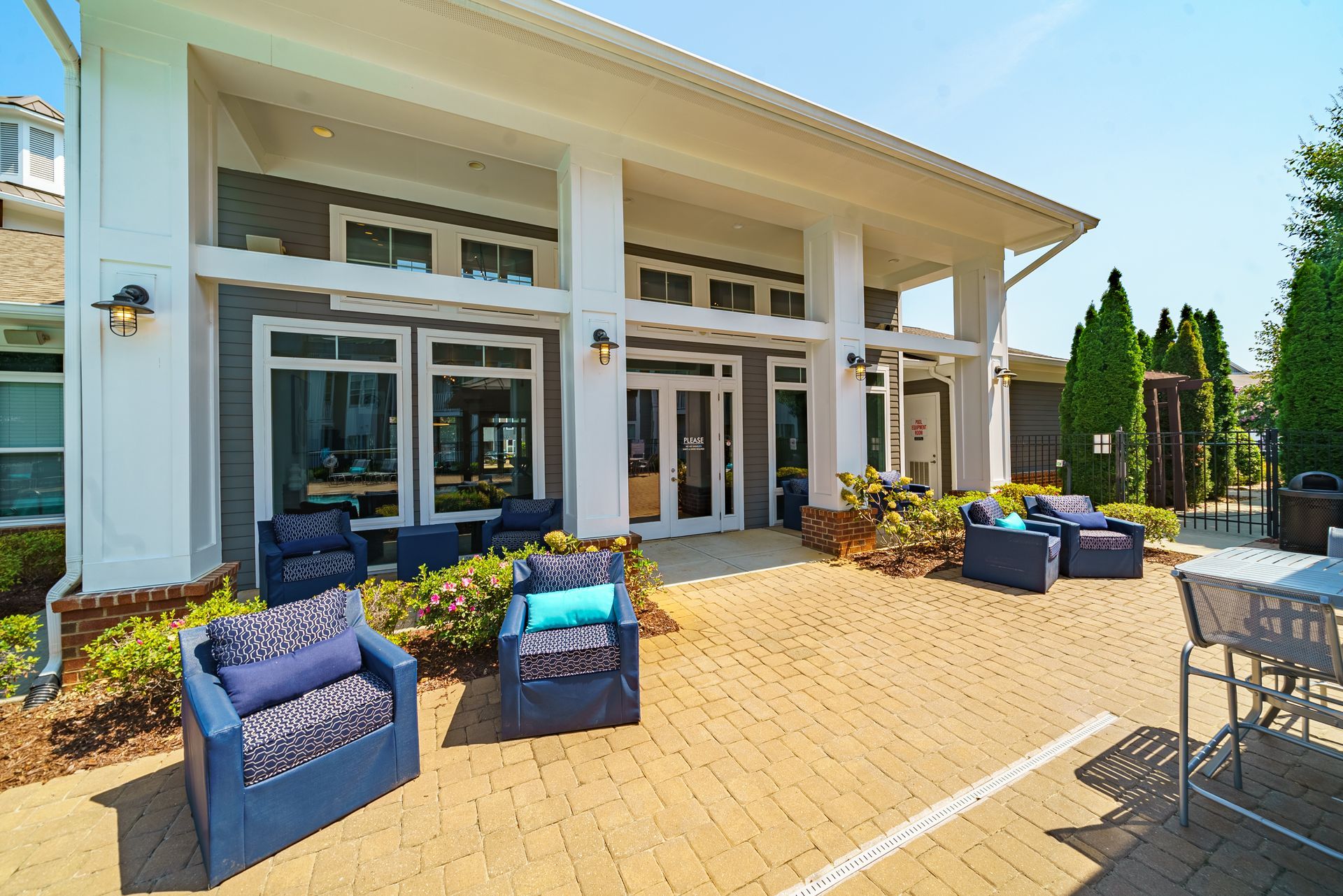 Outdoor patio with blue chairs and tables in front of a building with white columns and glass doors at Willows at Fort Mill, offers pet-friendly apartments for rent in Fort Mill, SC.