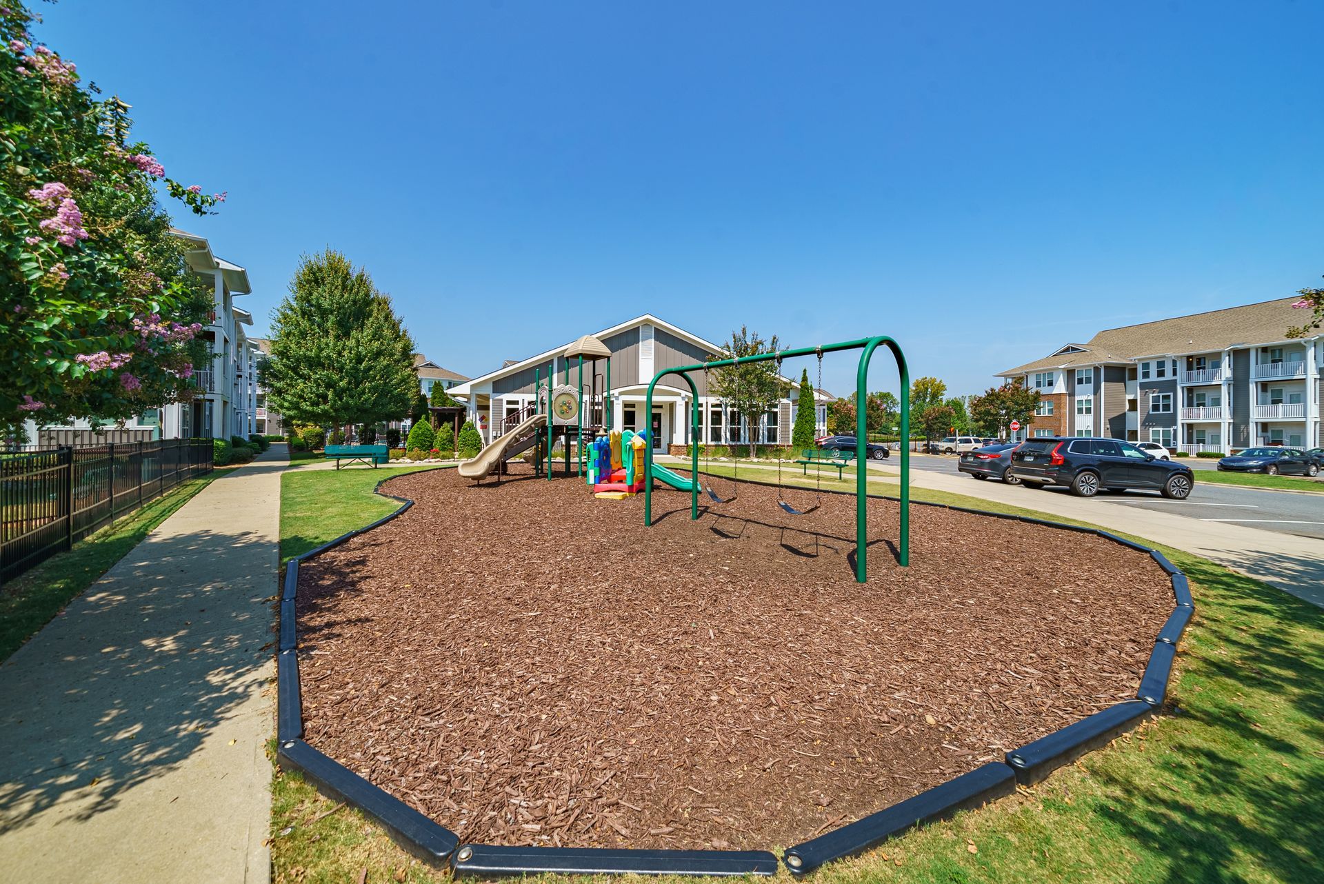 Playground with swings and slide surrounded by mulch in front of a building with apartments for rent near Kingsley Town Center in Fort Mill, SC, at Willows at Fort Mill.