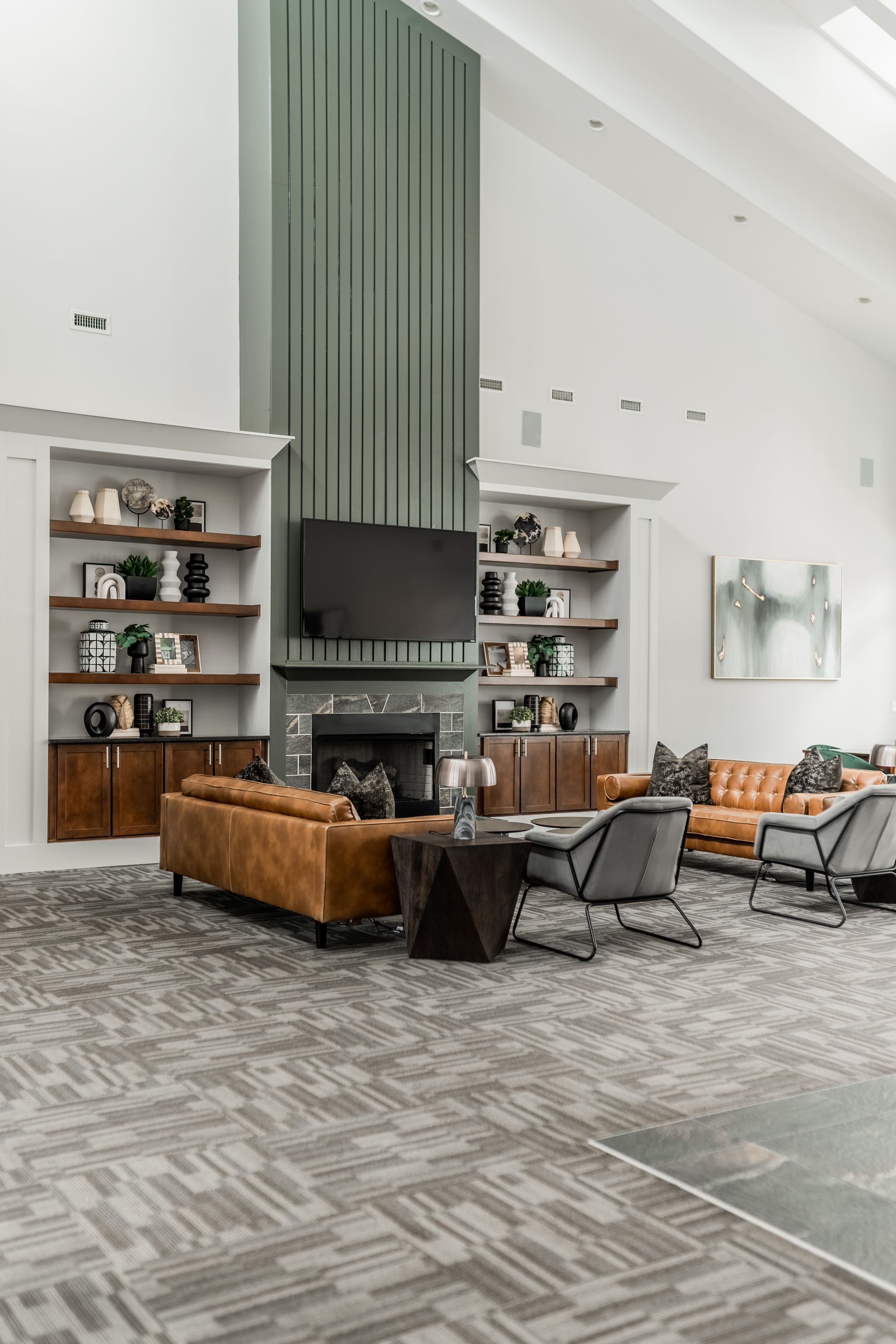 Lounge area with bookshelves, fireplace, leather sofas, and patterned carpet. Features a tall green accent wall at Willows at Fort Mill's clubhouse, offers 1,2, and 3 bedroom apartments in Fort Mill, SC.