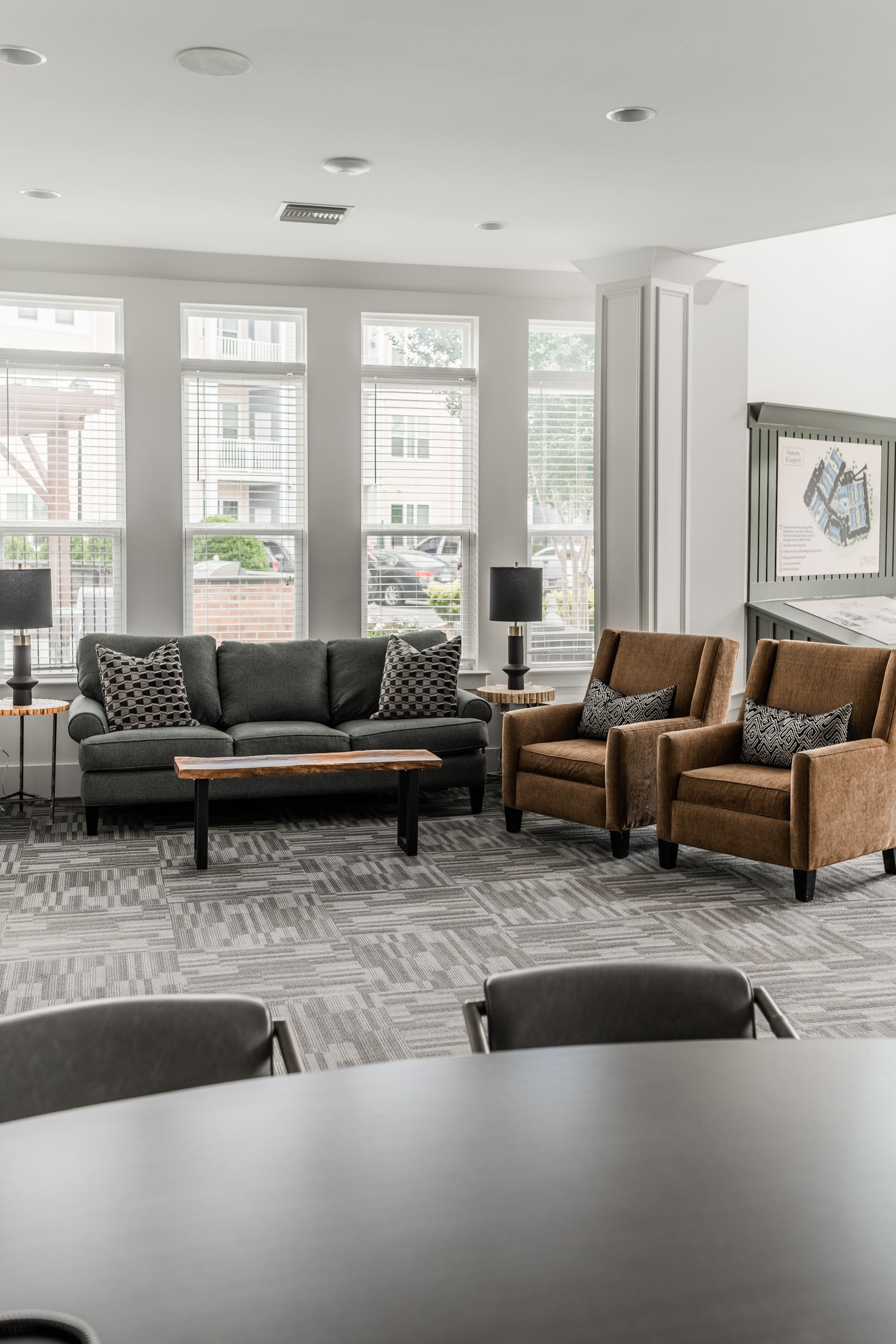 Resident lounge with gray sofa, two brown armchairs, rug, and large windows at Willows at Fort Mill, offers 1,2, and 3 bedroom apartments in Fort Mill, SC.