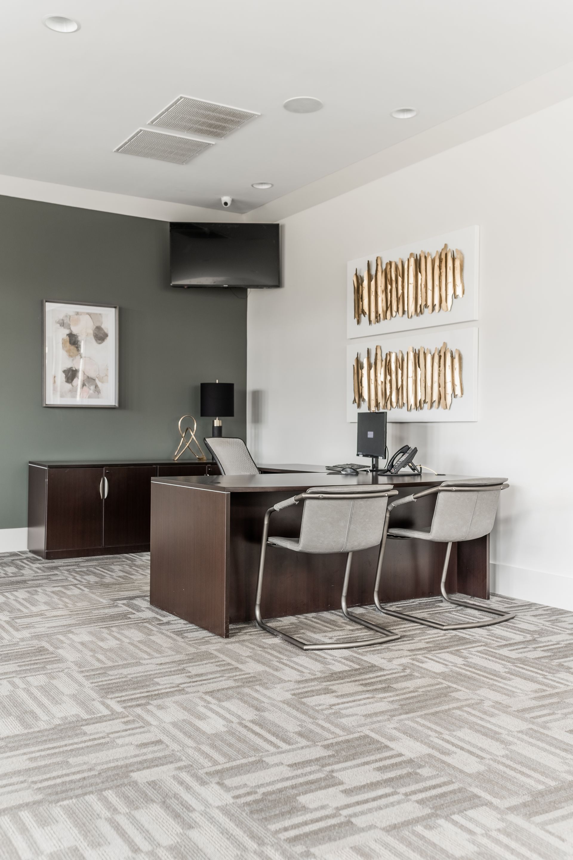 Office reception area with desk, chairs, artwork, TV, and a dark accent wall at Willows at Fort Mill, offers apartments in Fort Mill, SC.