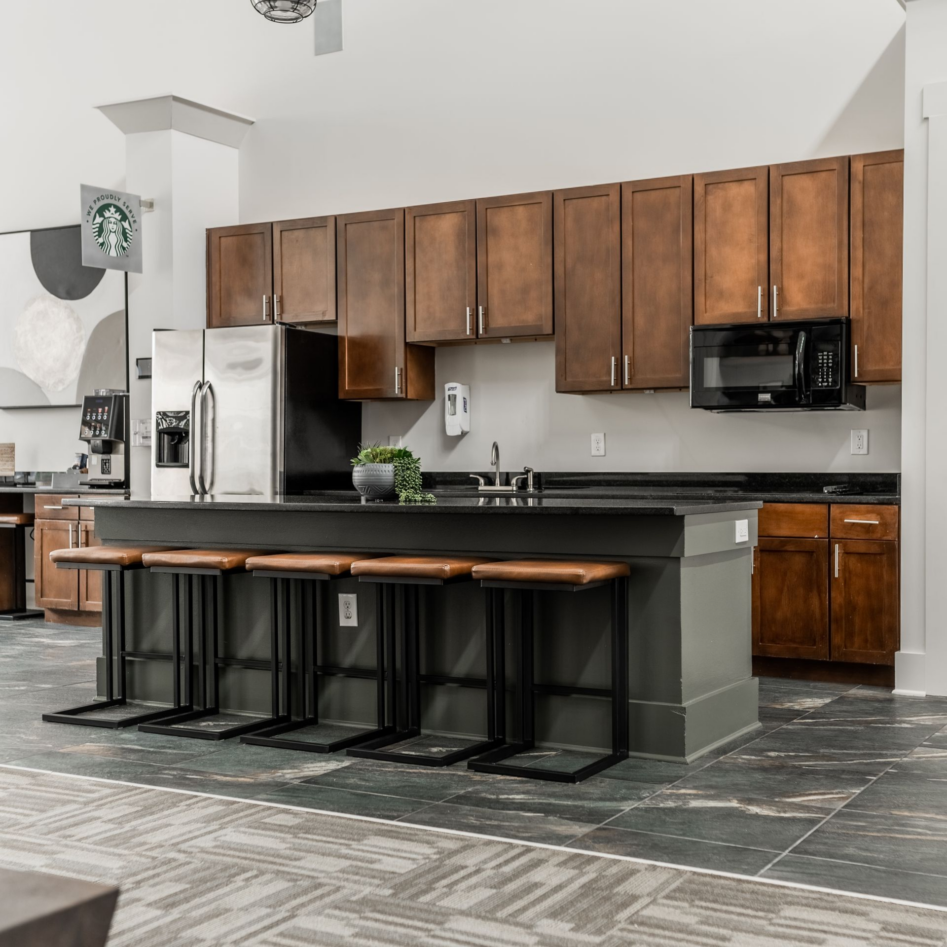 Kitchen with island and bar stools, dark brown cabinets, stainless steel appliances, and gray flooring at Willows at Fort Mill, offers 1,2, and 3 bedroom apartments for rent near Uptown Charlotte in Fort Mill, SC.