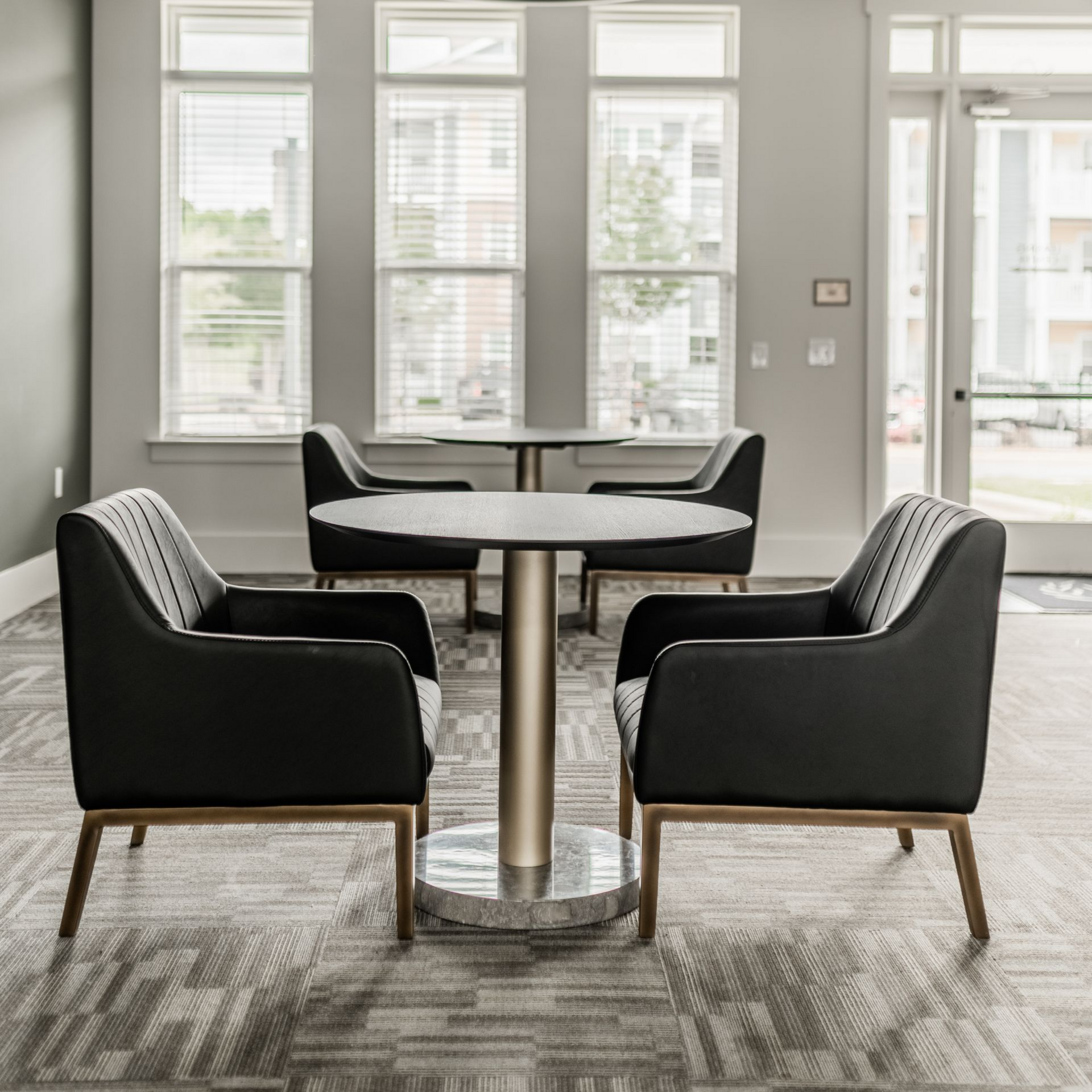 A seating area with chairs around a table, large windows, and a modern light fixture at Willows at Fort Mill's resident clubhouse, offers 1,2, and 3 bedroom apartments in Fort Mill, SC..