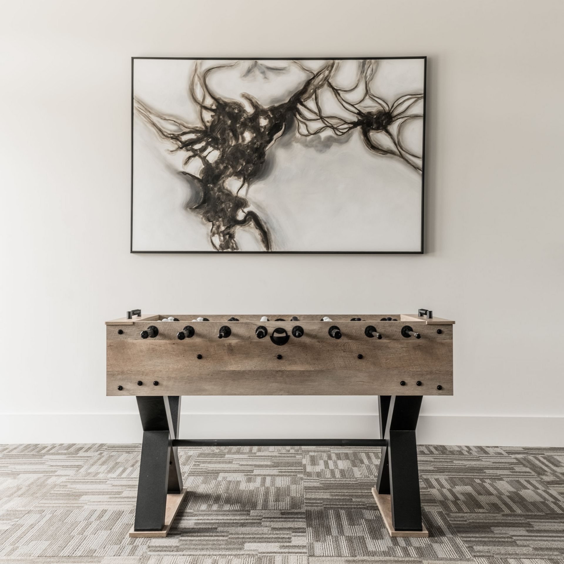 Foosball table beneath abstract art on a neutral-toned wall, set on patterned carpet at Willows at Fort Mill apartment community, offers 1,2, and 3 bedroom apartments in Fort Mill, SC.