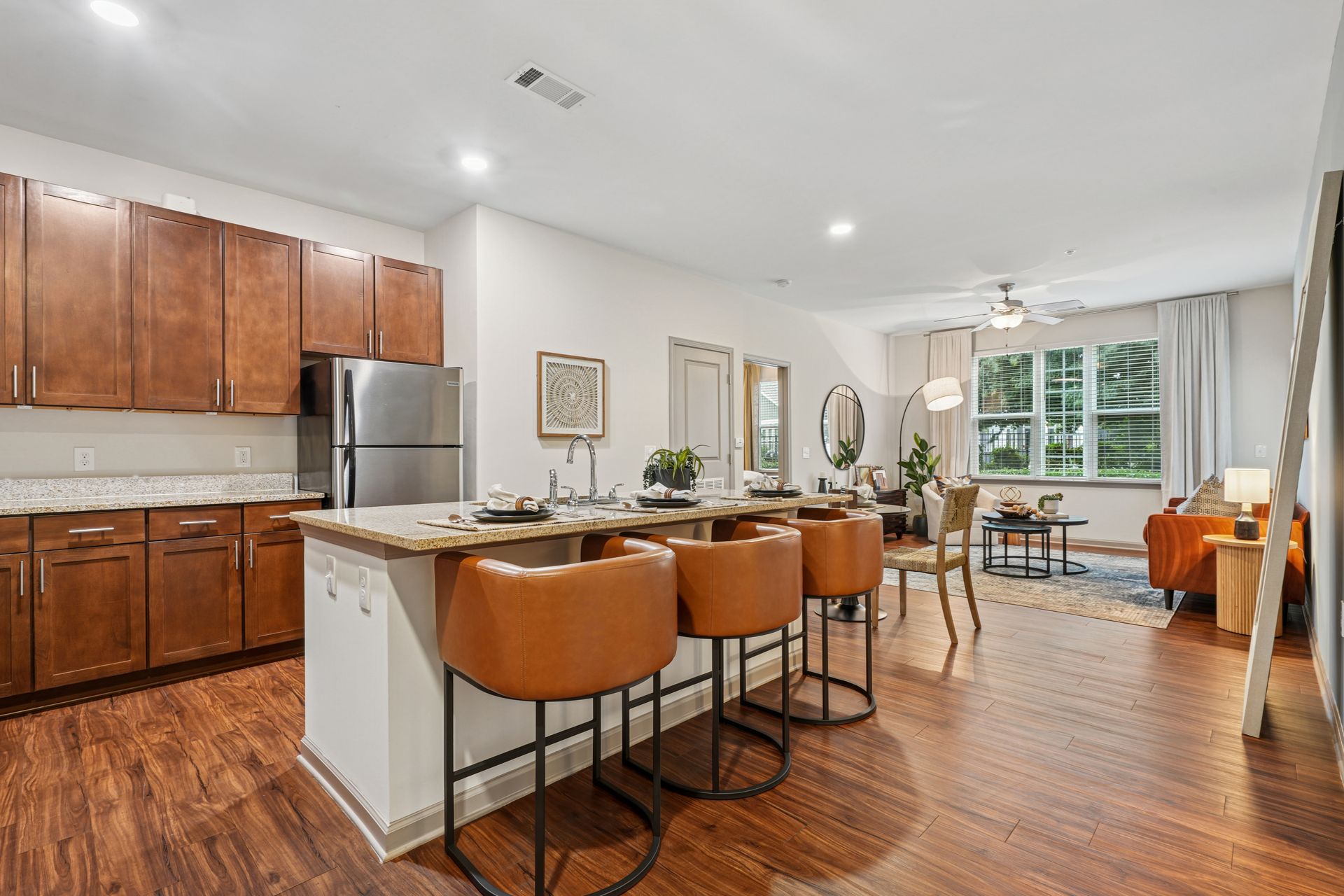 Kitchen with island and bar stools, leading to dining area and living room with orange couch at Willows at Fort Mill, offers apartments in Fort Mill, SC.