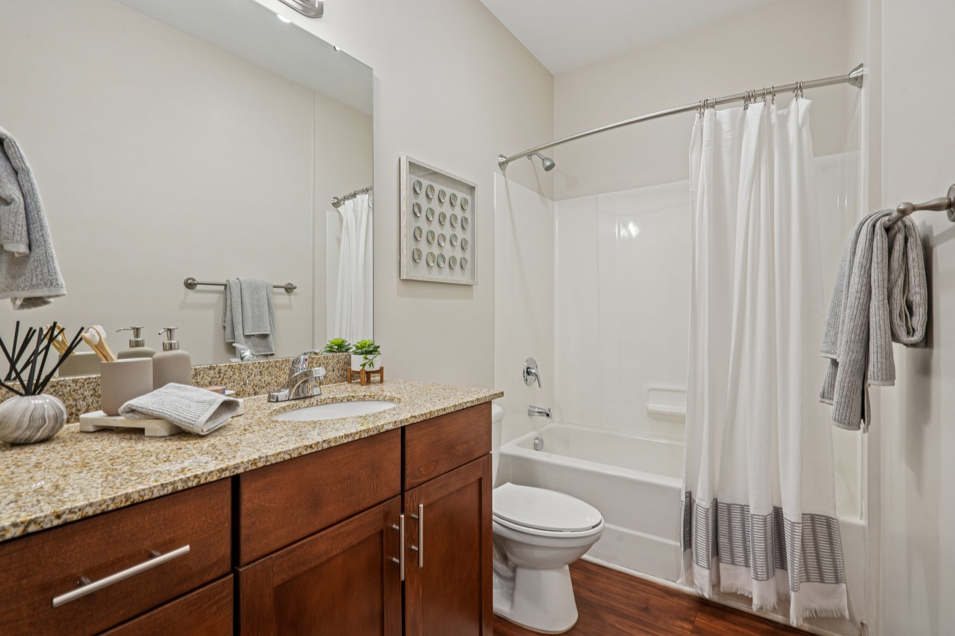 Bathroom with a vanity, toilet, and shower. Brown cabinetry, granite countertop, white fixtures, and wooden floors at Willows at Fort Mill, offers Fort Mill apartments for rent in SC.