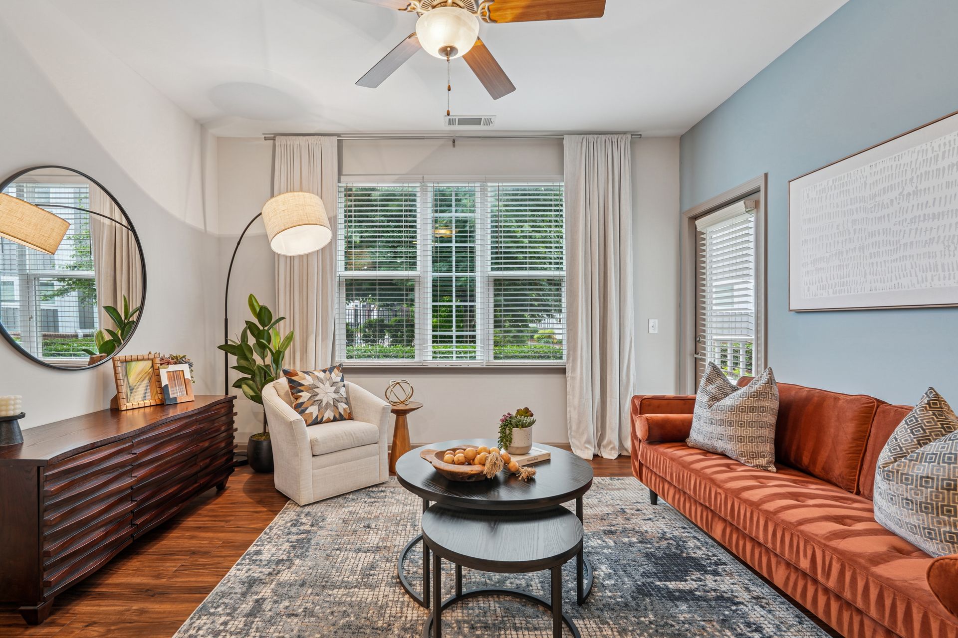 Living room with orange sofa, blue wall, round mirror, and dark wood floors at Willows at Fort Mill, offers Fort Mill apartments near Downtown.
