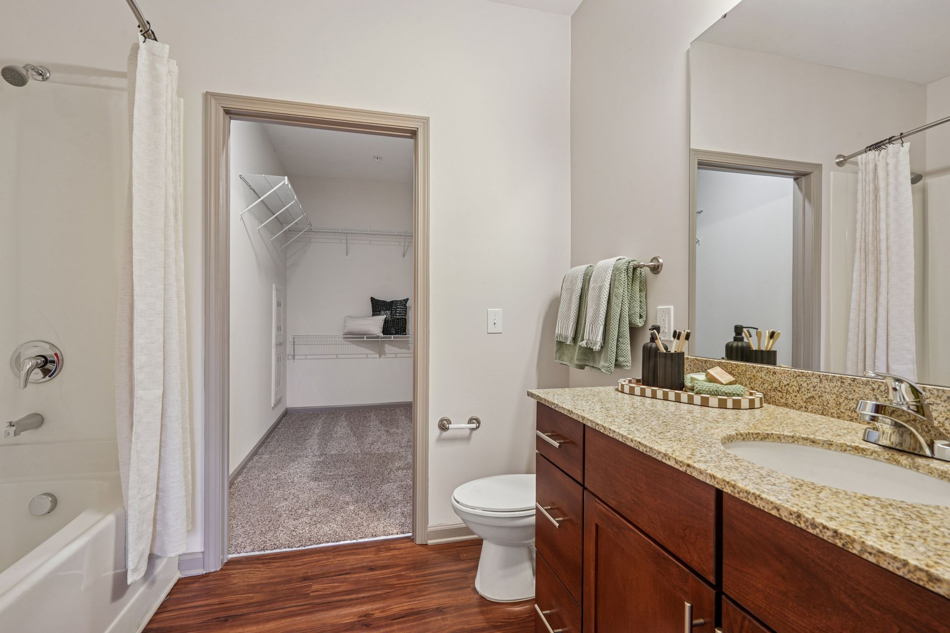 Bathroom with walk-in closet. Features a shower, sink, toilet, brown cabinets, and light granite countertop at Willows at Fort Mill, offers Fort Mill apartments for rent in SC.