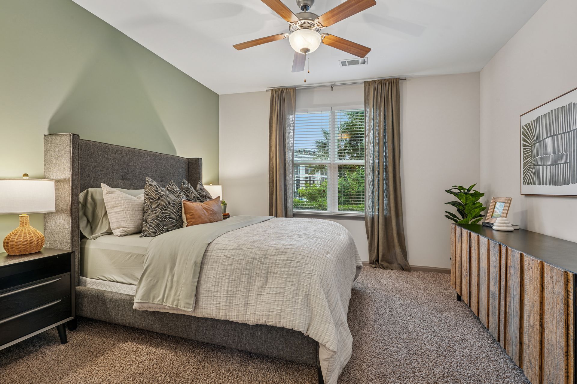 Bedroom with a bed, nightstand, dresser, window, and ceiling fan. Soft colors and neutral decor at Willows at Fort Mill, offers Fort Mill apartments near Downtown.