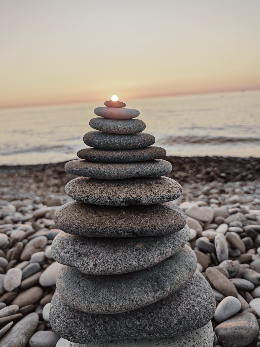 A stack of rocks on a beach with a candle in the middle.