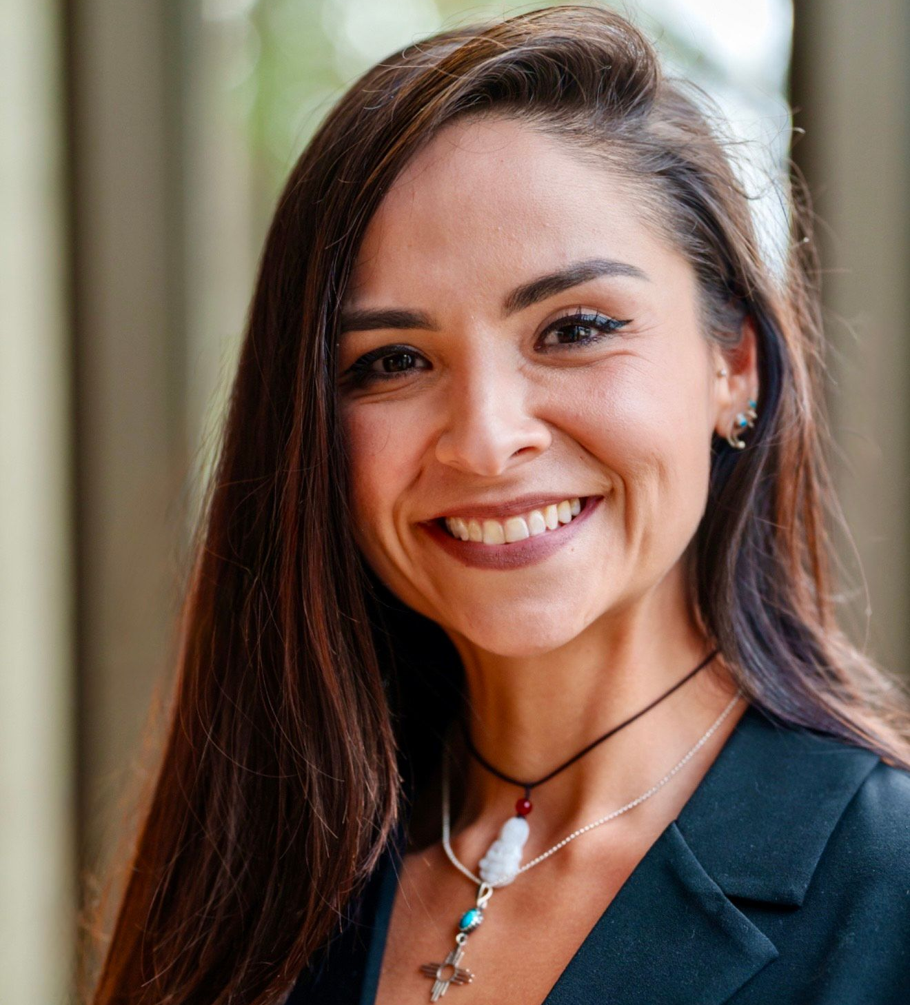 A woman wearing a green shirt and a gold necklace is smiling for the camera.