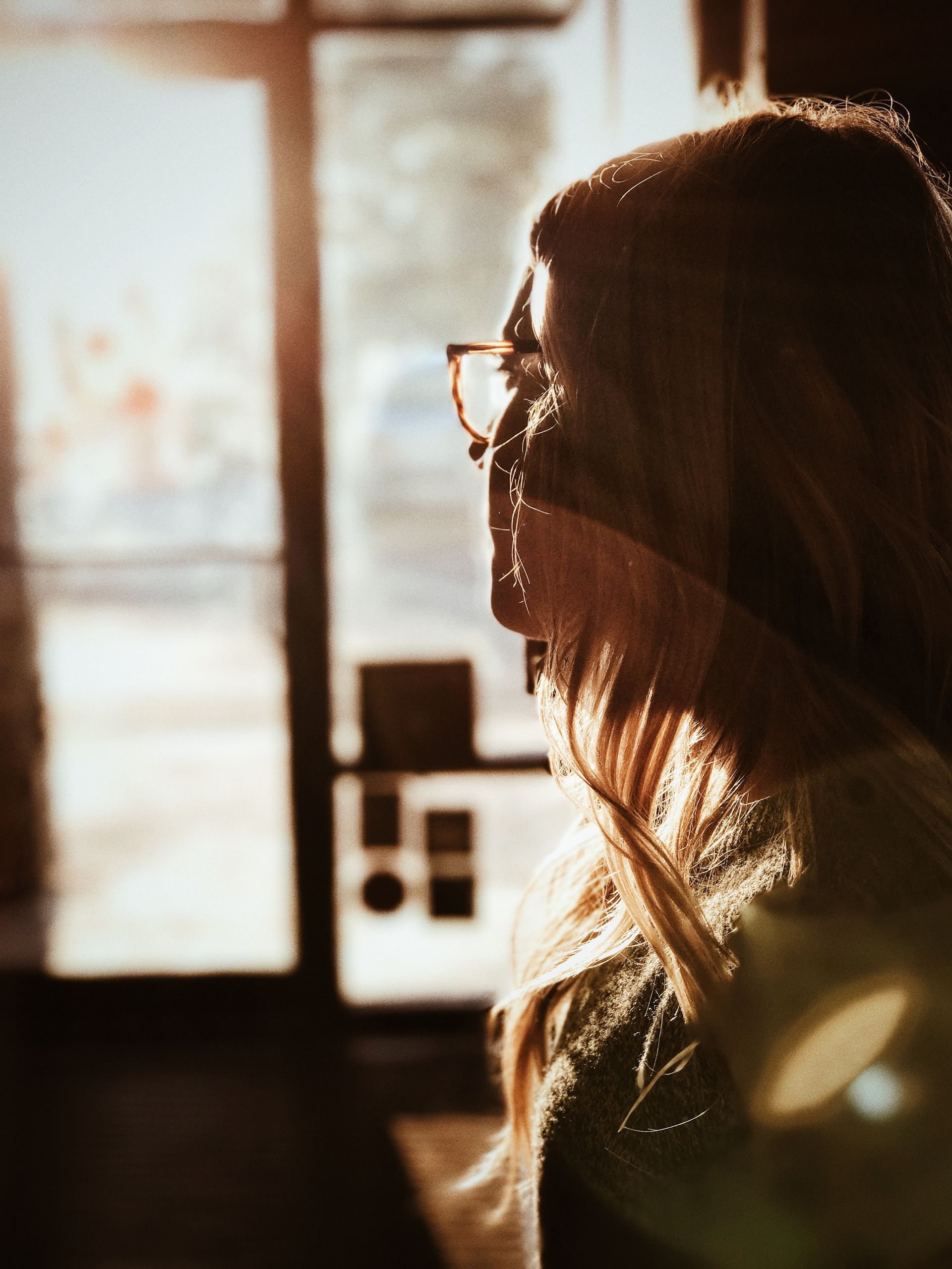 A woman wearing glasses is looking out a window