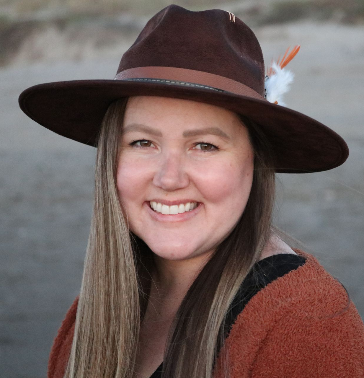 A woman wearing a brown hat with feathers on it is smiling.