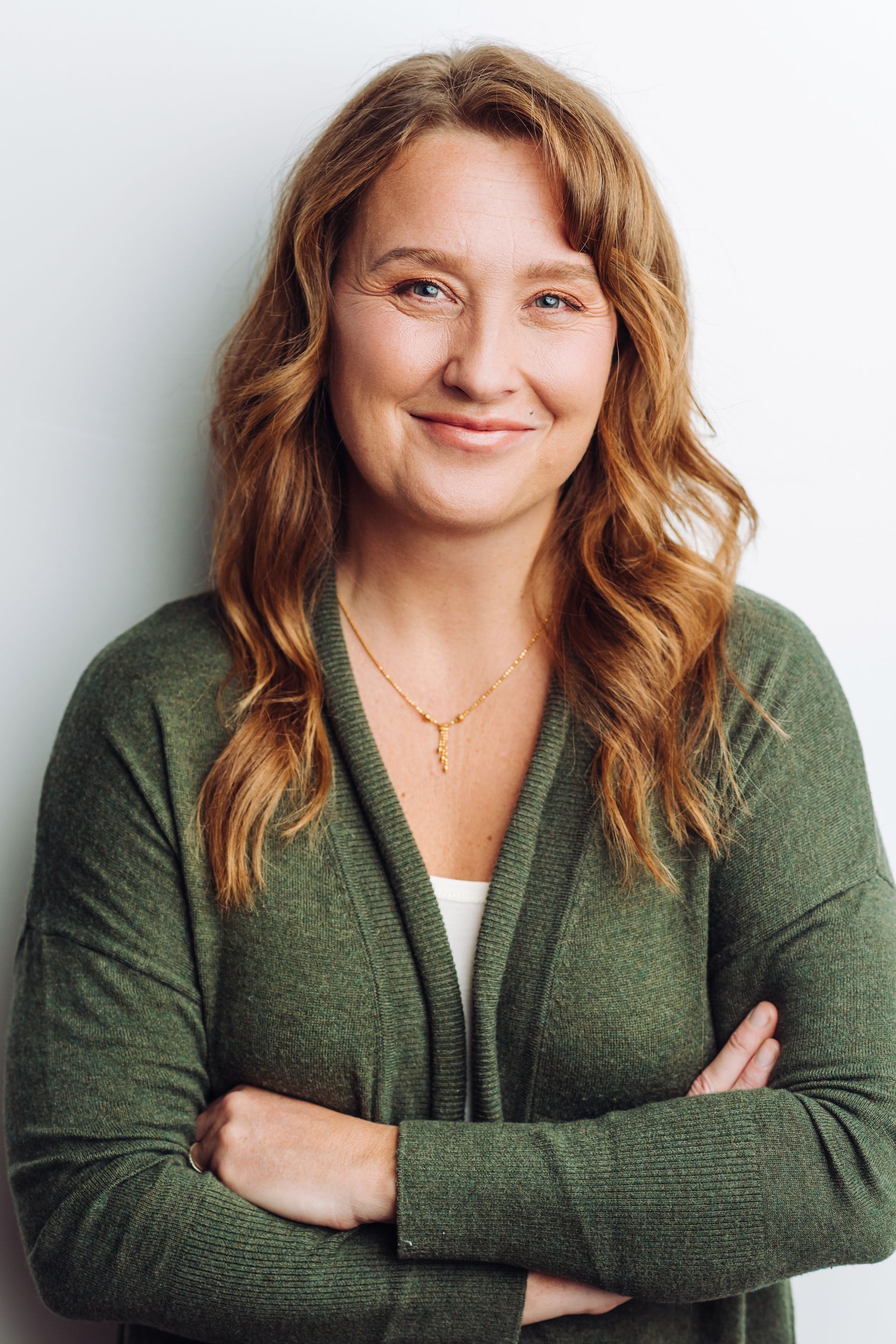 A woman in a green sweater is standing with her arms crossed and smiling.