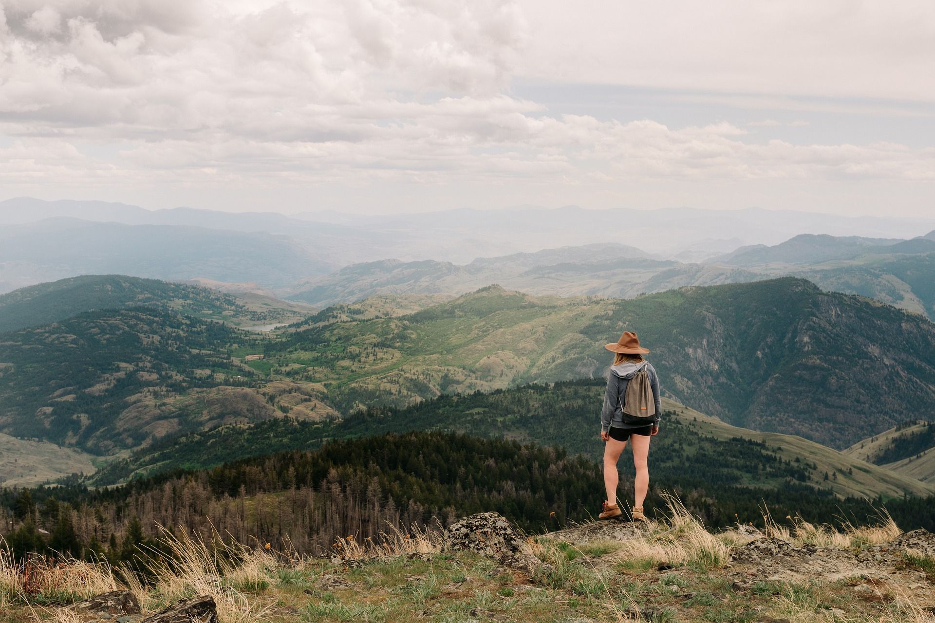 A person with a backpack is standing on top of a mountain looking at the mountains.