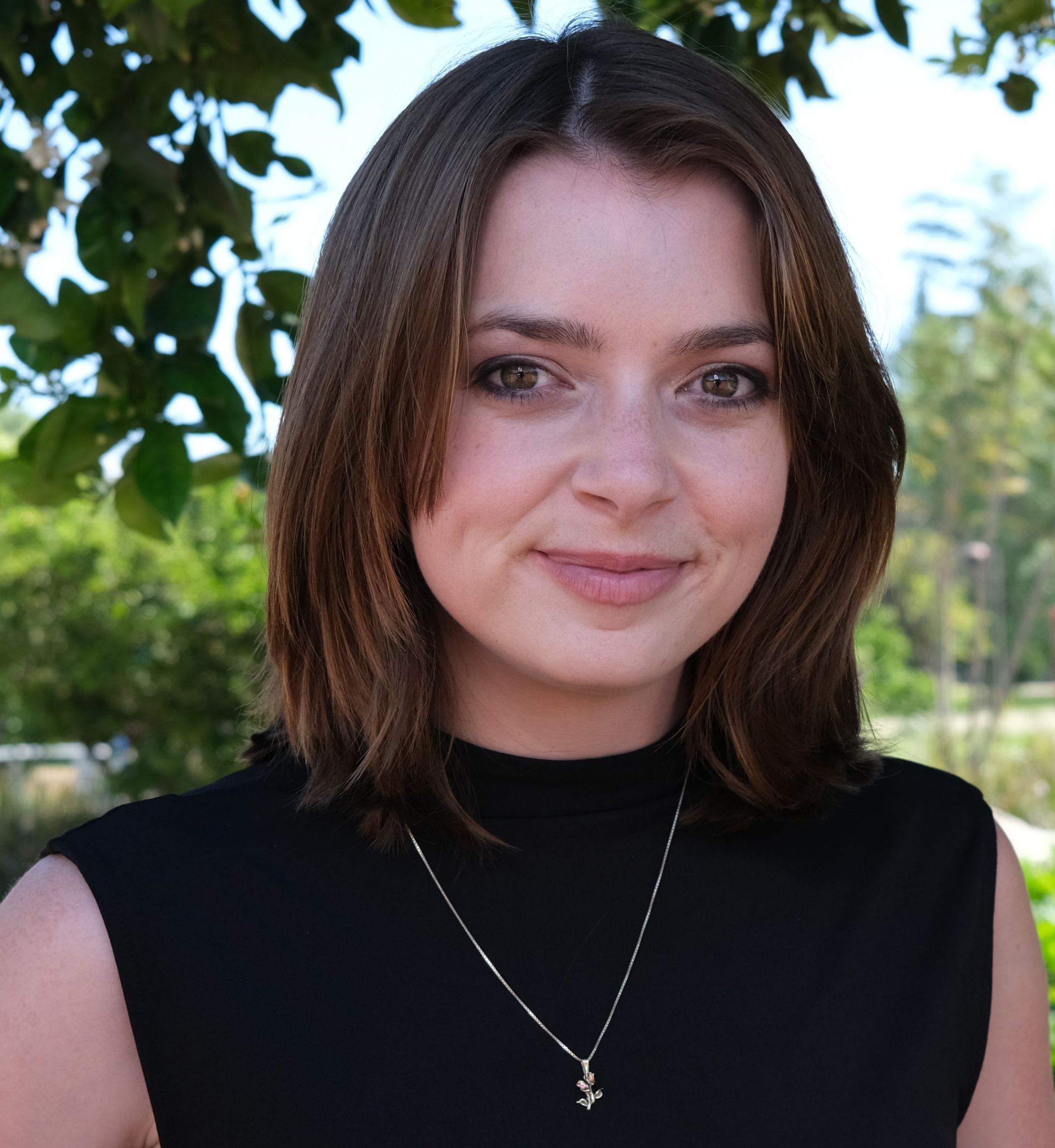A woman wearing a green shirt and a gold necklace is smiling for the camera.