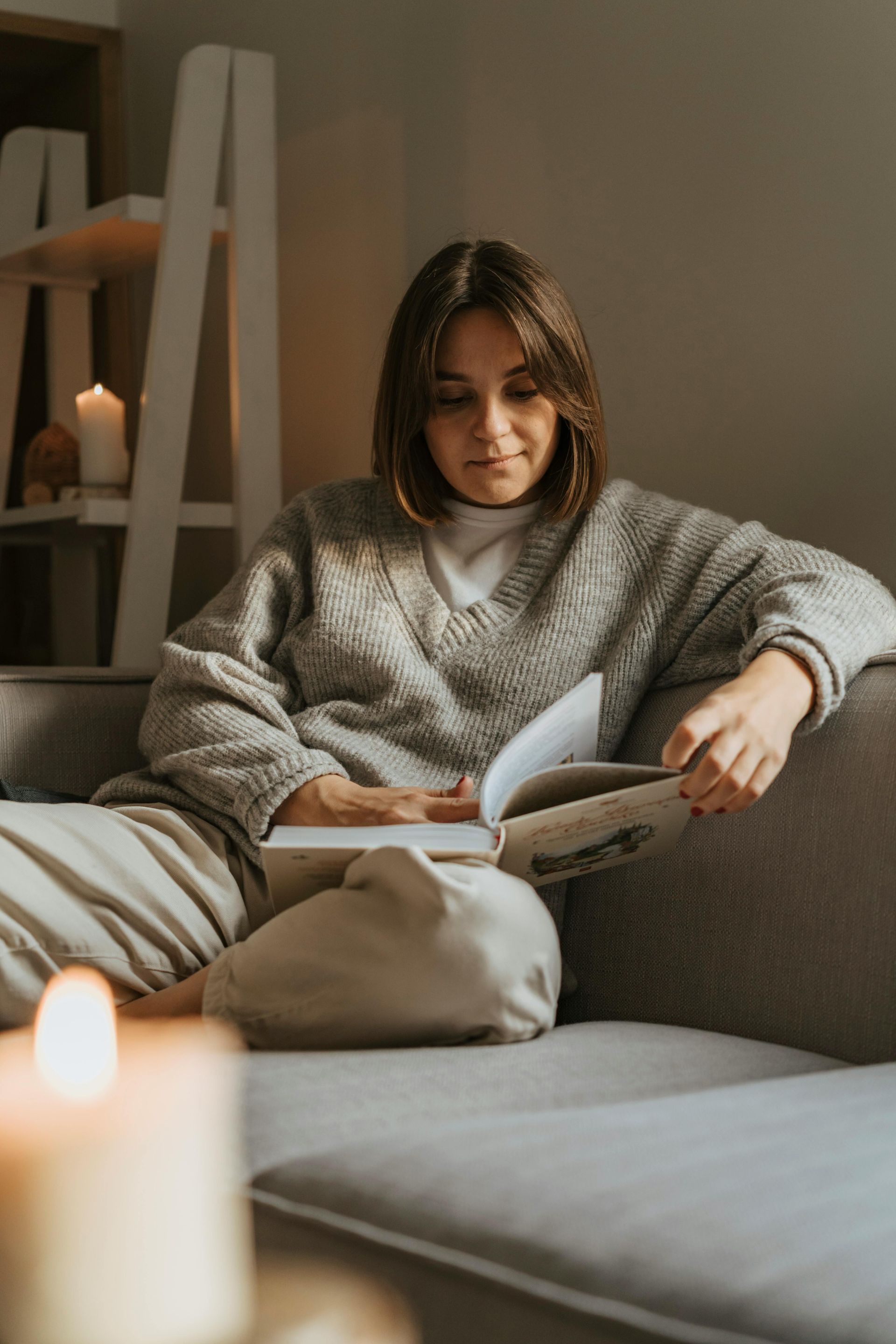 A woman is sitting on a couch reading a book.