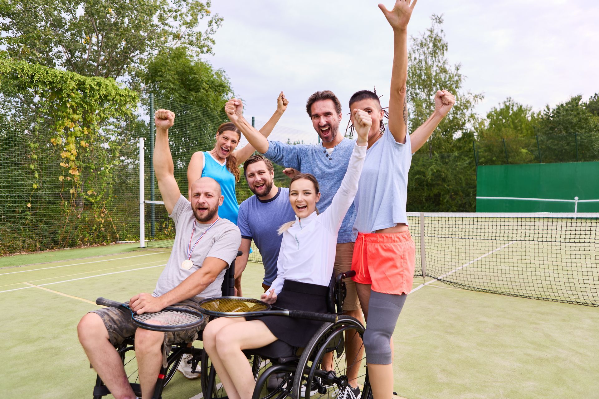 A group of people are standing on a tennis court with their arms in the air.