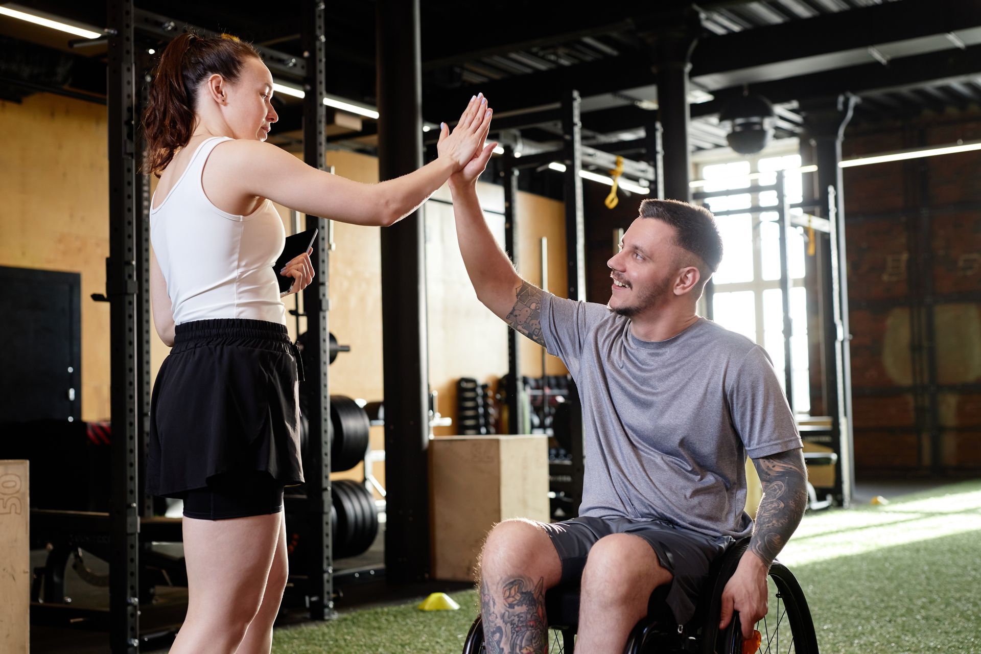 A man in a wheelchair is giving a woman a high five in a gym.