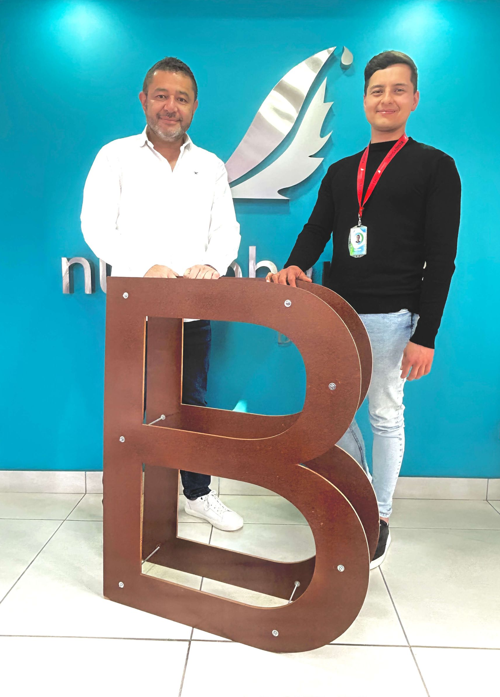 Gerente general de Laboratorios Nutripharma junto al coordinador de SST y Medio Ambiente sostienen la B viajera frente al logo de Nutripharma.