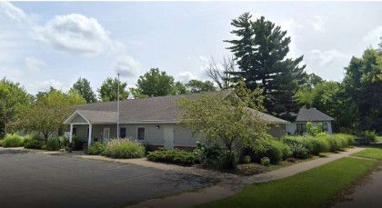 A white house with a gray roof is surrounded by trees and bushes.