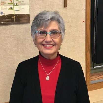 A woman wearing glasses and a red sweater is smiling for the camera.