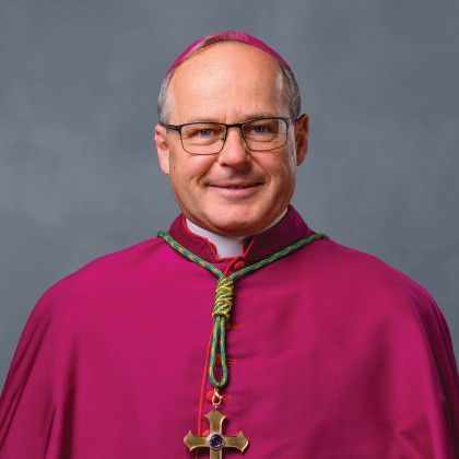 A man wearing glasses and a purple cape with a cross around his neck.