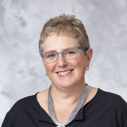 A woman wearing glasses and a necklace is smiling for the camera.