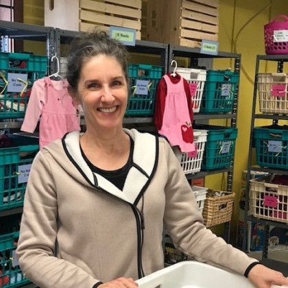 A woman is standing in front of a shelf full of baskets and clothes.