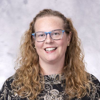 A woman with curly hair and glasses is smiling for the camera.