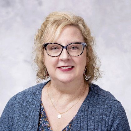 A woman wearing glasses and a blue sweater is smiling for the camera.
