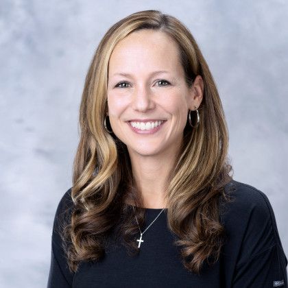 A woman wearing a black shirt and a cross necklace is smiling for the camera.