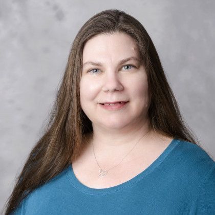 A woman with long hair is wearing a blue shirt and a necklace.