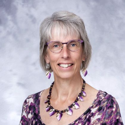 A woman wearing glasses and a purple necklace is smiling for the camera.