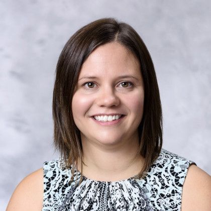 A woman is smiling for the camera and wearing a blue and white top.