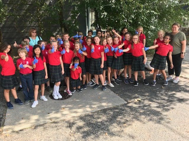 A group of children wearing red shirts and blue gloves are posing for a picture.