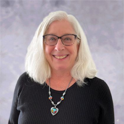 A woman wearing glasses and a necklace is smiling for the camera.