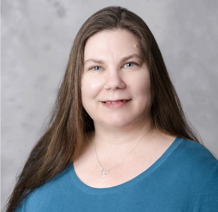 A woman with long hair is wearing a blue shirt and a necklace