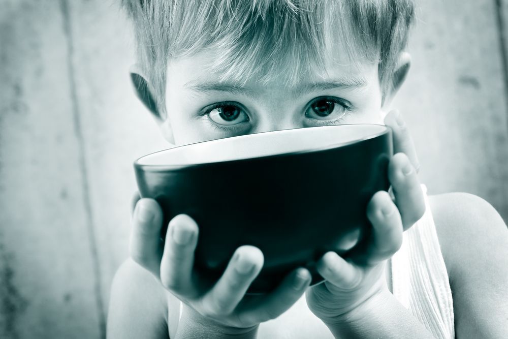 A young boy is holding a bowl in front of his face.