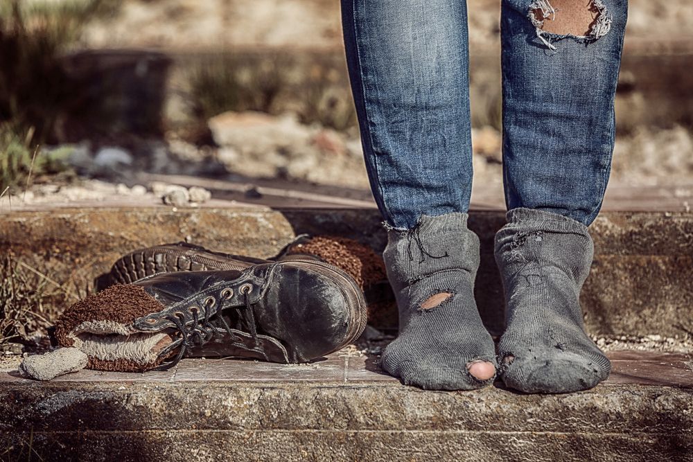 A person wearing dirty socks and ripped jeans is standing on a set of stairs.